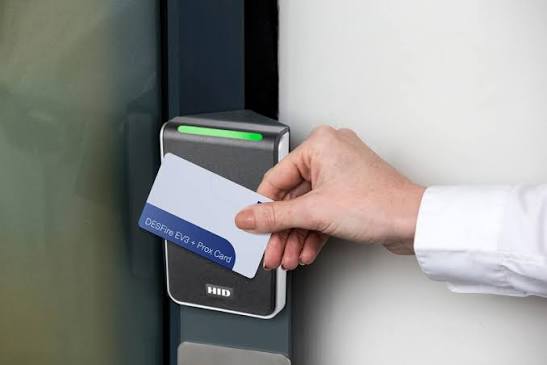 Hand holding a HID proximity card up to a card reader mounted beside a door