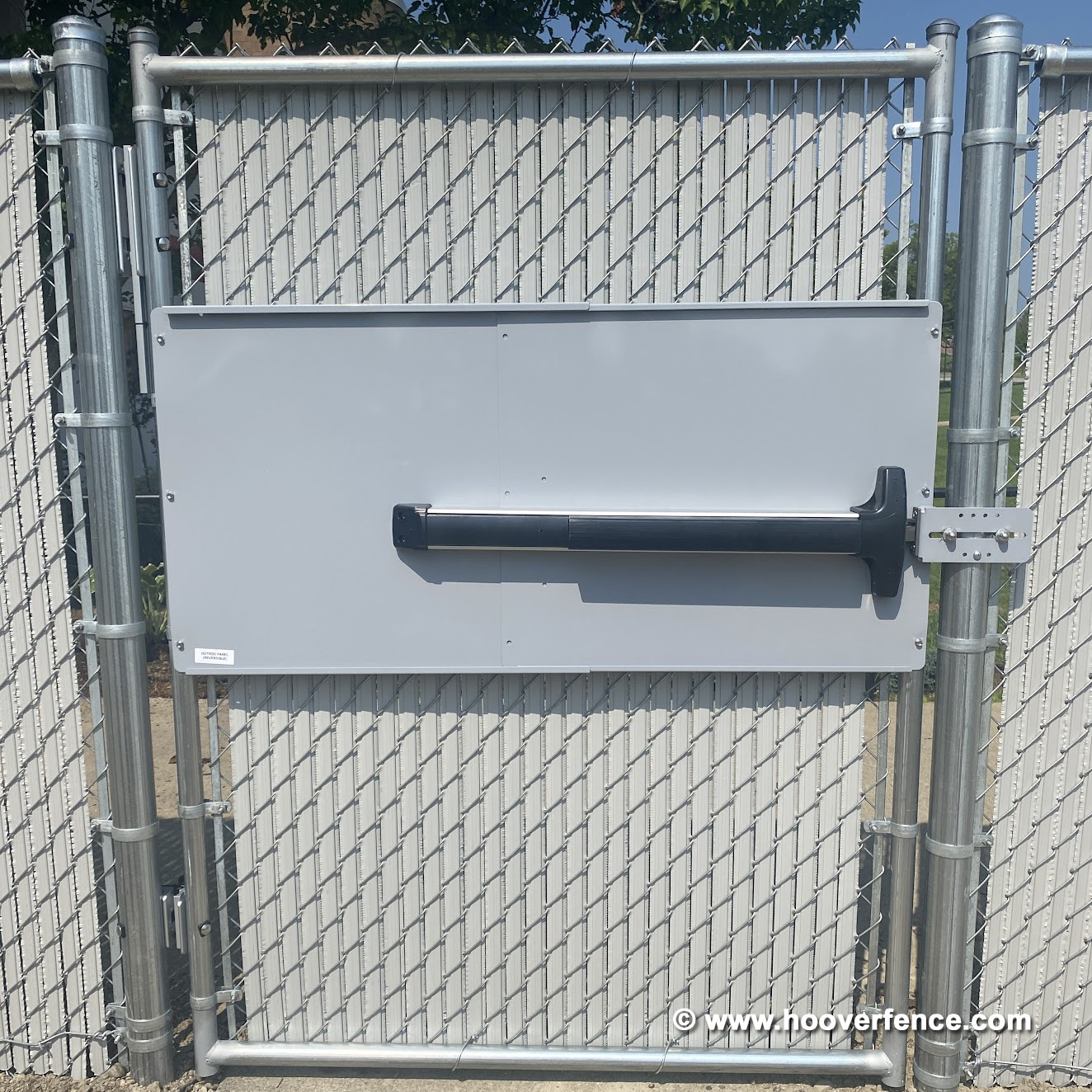 Panic exit bar with flush latch mounted on a metal panel on a chain-link gate
