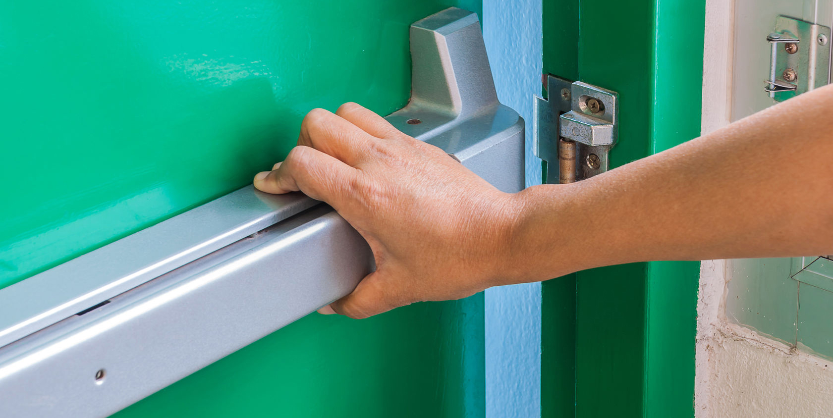 Hand pressing the panic exit bar on a green commercial door