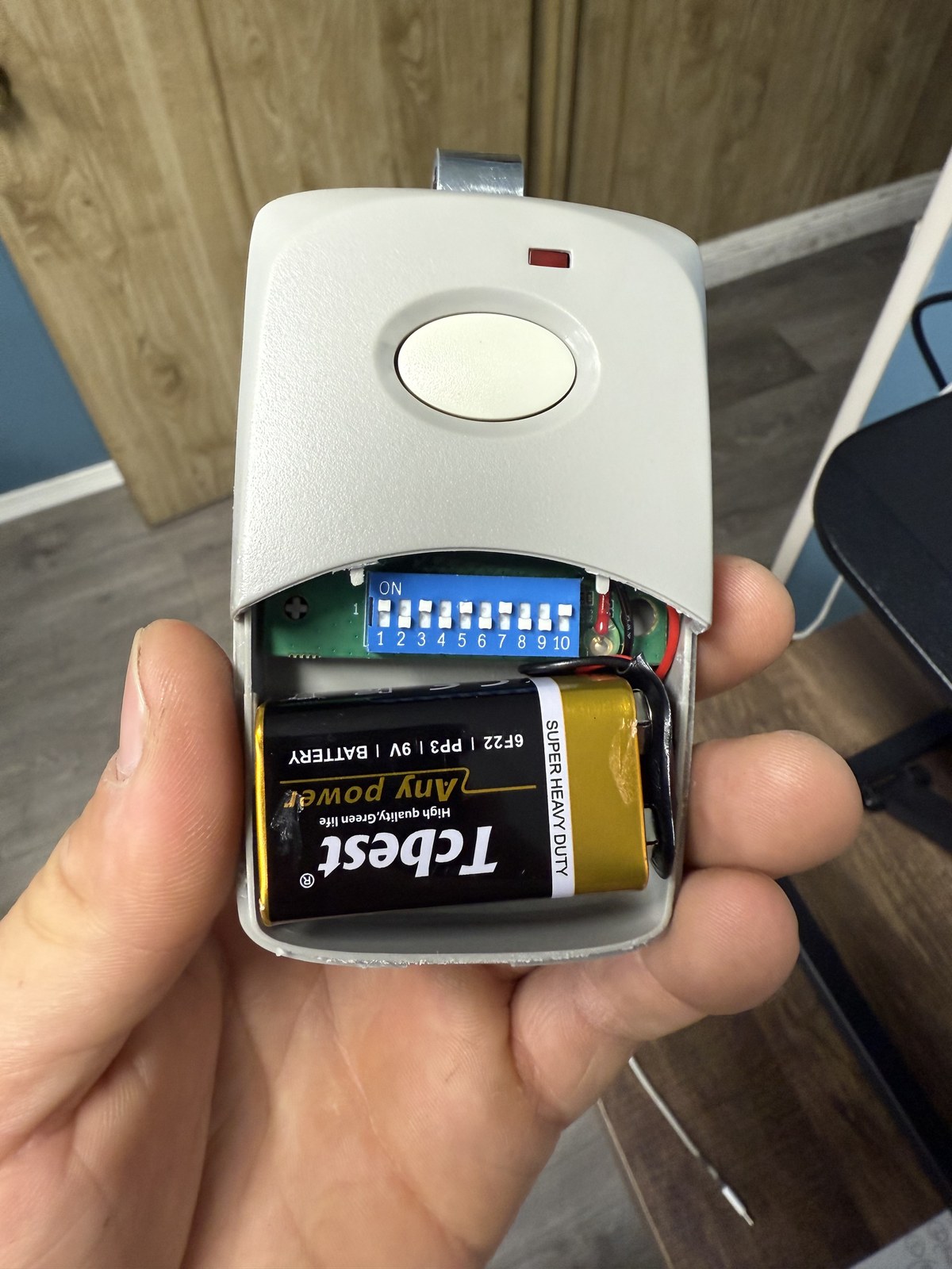 Hand-held gate remote opened to show its DIP switches and battery
