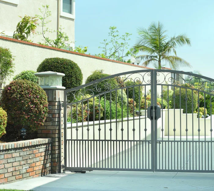 Ornamental iron double swing gate between brick pillars, with the in-ground operator concealed at the base