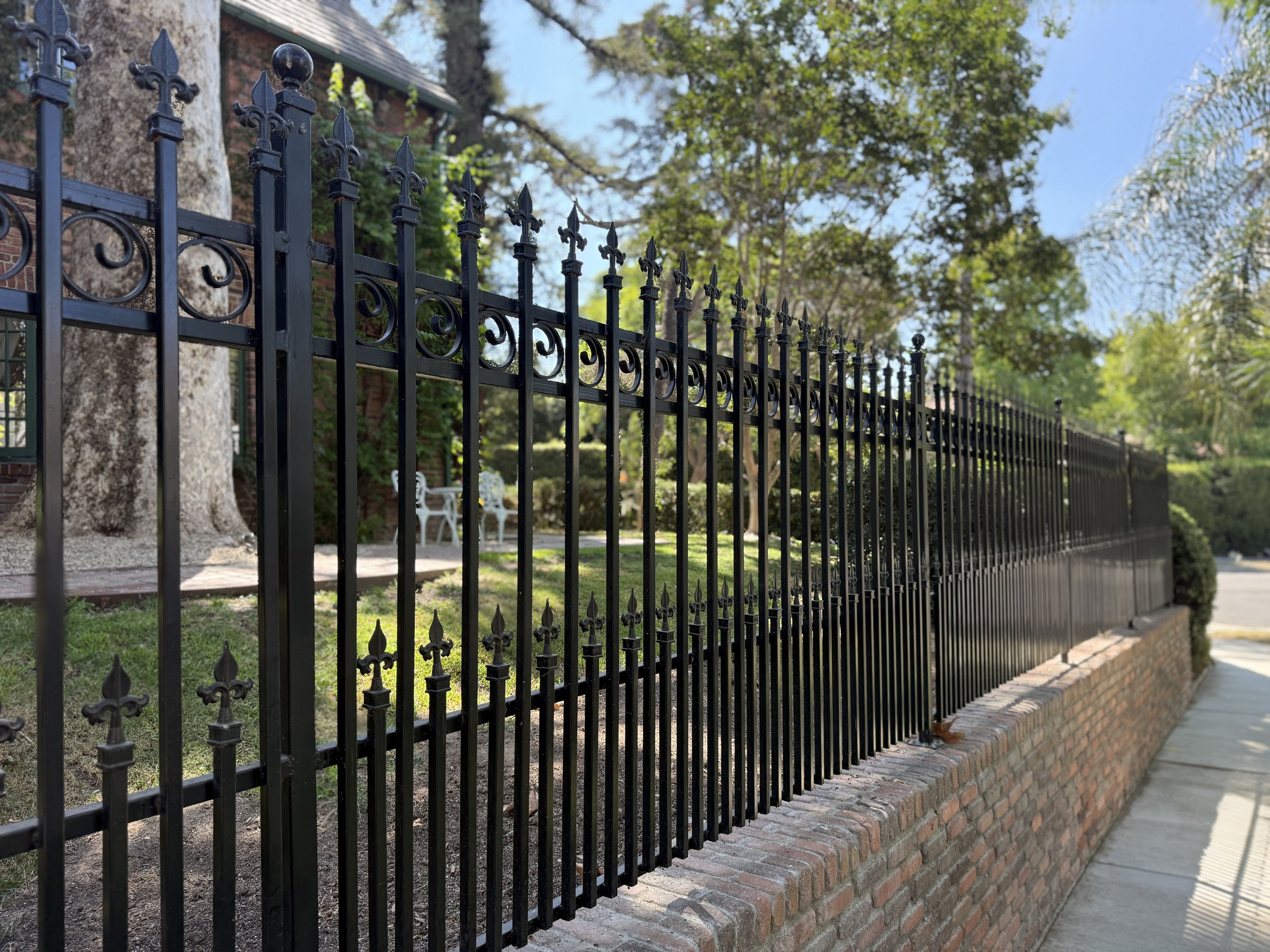 Ornamental iron fence line with finial posts running along a brick wall